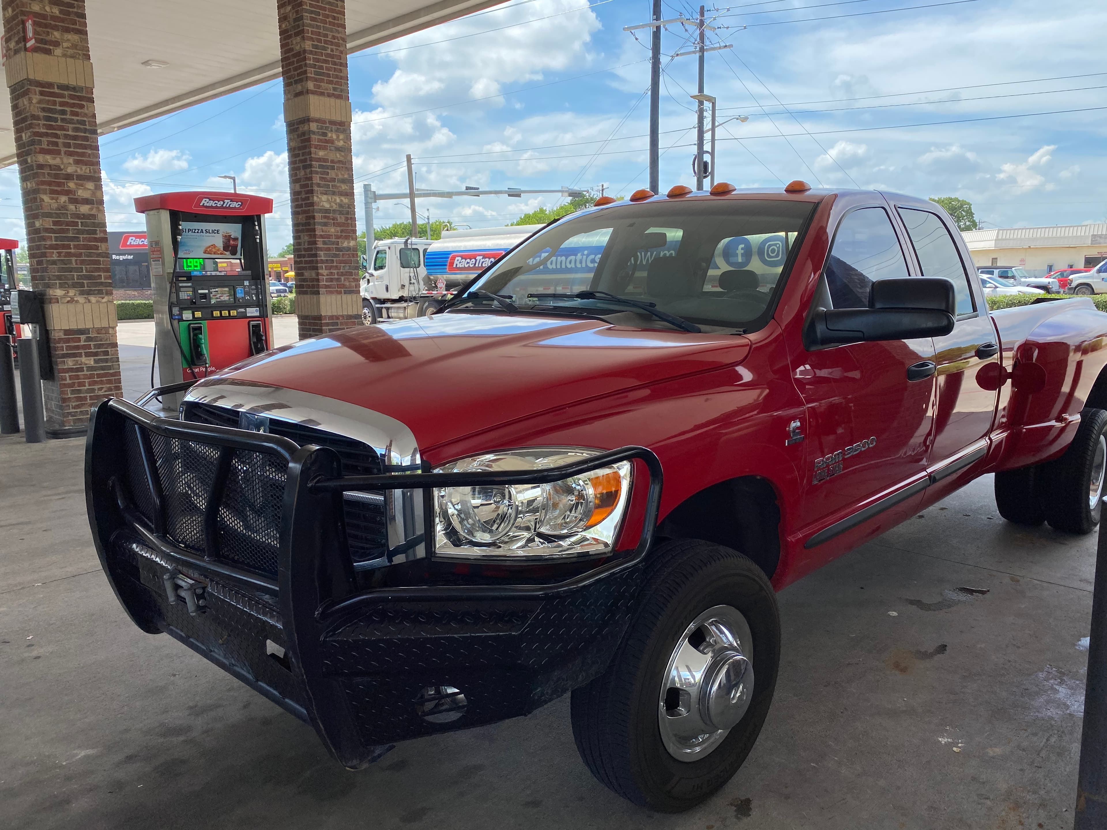 Red Dodge Ram 3500 pickup truck with a black brush guard at a gas station.